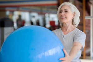 One more time. Glad senior charming woman smiling and holding fit ball while exercising in a gym