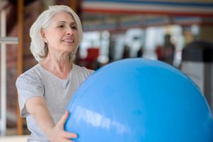 One more time. Glad senior charming woman smiling and holding fit ball while exercising in a gym